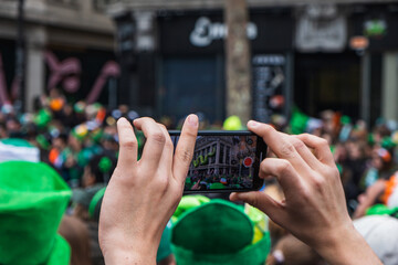 Hand with phone, taking picture of the parade, green costume and green hats, people, Paddy's day Dublin centre, Ireland - obrazy, fototapety, plakaty
