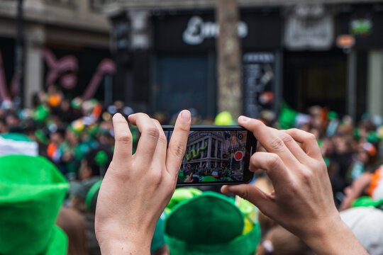 Hand with phone, taking picture of the parade, green costume and green hats, people, Paddy's day Dublin centre, Ireland