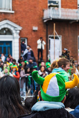 Green hat in the crowd, people in the street with costumes, irish flag colours, Paddy's day parade...