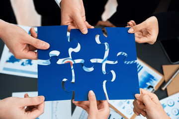 Closeup top view business team of office worker putting jigsaw puzzle together over table filled...