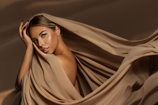 Beautiful Girl Face with Natural Makeup and Sun Tanned Skin. Beauty Woman wrapped in Brown Silk Fabric waving on Wind. Fashion Model Portrait wearing Head Satin Scarf - Powered by Adobe