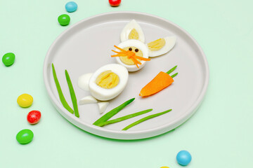Easter funny creative healthy breakfast lunch food idea for kids, children.Bunny, rabbit made from boiled chicken eggs,peeled carrots, greens on plate green table background.Top view Flat lay