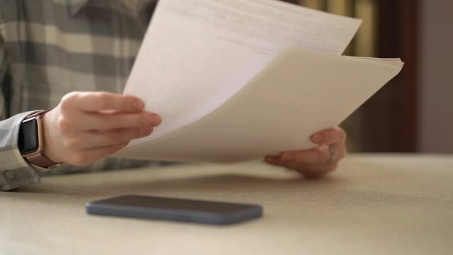 Woman's hands hold paper documents. The girl looks at the bills sitting at the table at home.