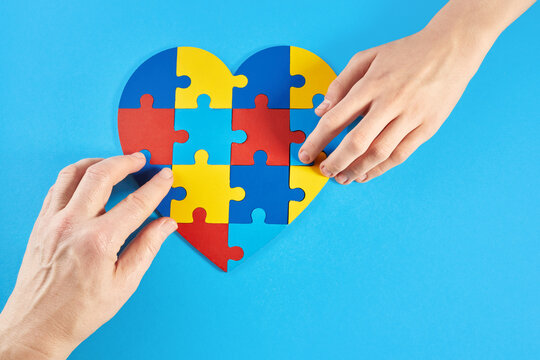 Father and autistic son hands holding jigsaw puzzle heart shape. World Autism Awareness Day