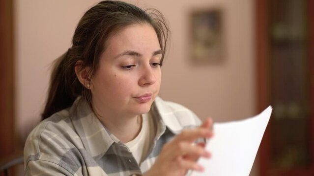 Stressed woman looking at bills and holding her head while sitting in room at home.