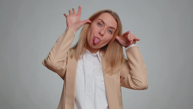 Portrait of young businesswoman making playful silly facial expressions and grimacing, fooling around, showing tongue. Female girl in formal suit. Pretty woman isolated on gray studio background