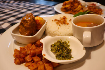 A Complete Dish of Padangnese Food with Rendang, Spicy Potato, Rice, Green Chilies, and Vegetable Curry Soup from Indonesia