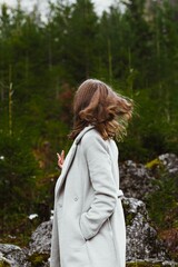 Vertical shot of a young Caucasian female walking in a forest wearing a white coat