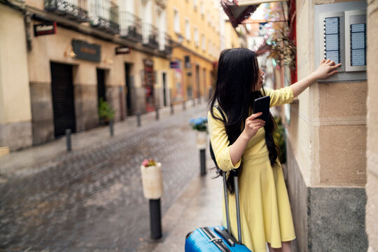A tourist girl with her suitcase knocking on the door of a tourist flat.
