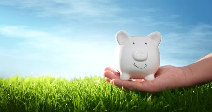 Hand with piggy bank on grass