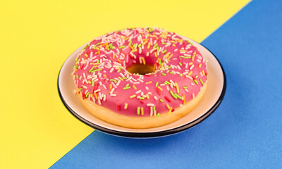 Pink donut in a white saucer on yellow and blue background