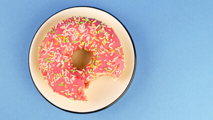 Bitten pink donut in a white saucer on a blue background