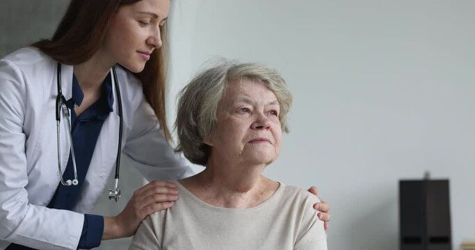 Pretty female geriatric doctor looking at serious silent elder patient with sympathy, care, touching shoulders, hugging senior thinking woman with healthcare problem, mental disease