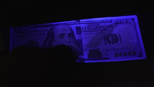 verification of counterfeit money in ultraviolet. UV check of USD banknotes. Money falsification concept background. In-depth inspection equipment. Equipment for in-depth inspection of money