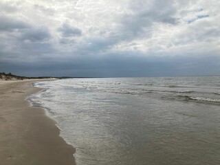 Fototapeta na wymiar Beautiful seascape of calm ocean waves crashing on the sandy shore on a cloudy day