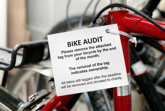 Bike audit tag attached to a bicycle with defocused bike room of strata building. Bicycle amenity audit tag with detailed instructions. Used to find unclaimed and forgotten bikes. Selective focus.