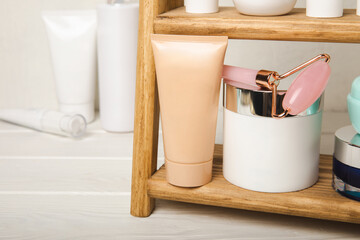 Shelf with care cosmetics in the bathroom against a white wall. Washing gel, toner, serum and body cream, gua sha massage roller, shampoo and hair balm. Decorative and care cosmetics.Beauty concept.