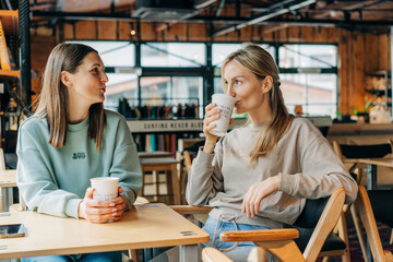 Two attractive women are discussing and drinking coffee in a coffee shop.