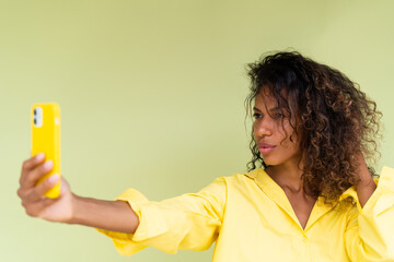 Beautiful african american woman in casual shirt on green background happy taking photo selfie on smart phone