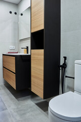 Vertical. Minimalist bathroom. Toilet, column and sink cabinet in the background, porcelain walls and floors. Black faucets.