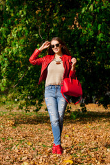 Young woman in fashion red jacket and blue jeans in autumn park