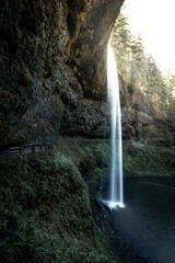 Fototapeta na wymiar Vertical shot of the beautiful waterfall surrounded by dark mossy rocks.