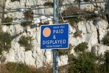 Fototapeta premium Blue pay and display car park sign with rocks in the background.