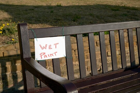 Brown wooden bench with a wet paint sign on it.