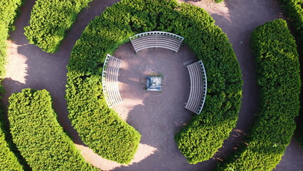 An aerial view of concentric ornate bushes with benches in the center