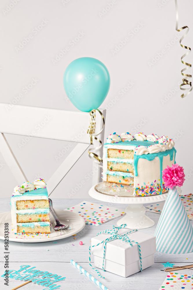 Wall mural birthday party table setting with slice of vanilla confetti cake and decorations on a light grey whi