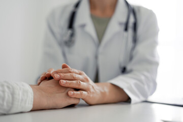 Doctor and patient sitting at the desk in clinic office. The focus is on female physician's hands...
