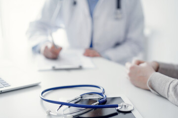 Stethoscope lying on the tablet computer in front of a doctor and patient at the background . Medicine, healthcare, reasuring hands concept