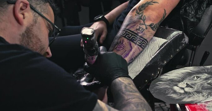 Close up tattoo artist shows the process of getting black tattoos with paint. The master works in black sterile gloves. Master tattoo artist in studio.