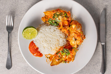Delicious Brazilian fish moqueca with tomato, onion, olive oil, coriander and orocum seed. Served on a white porcelain plate with rice.