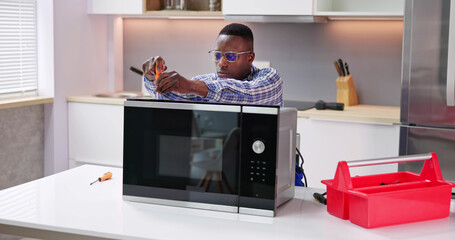 Male Serviceman Using Screwdriver To Repair Microwave