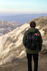 Young Male Tourist Hiking with Backpacks on Top of Rocky Canyon Valley in Front of a city Goreme Cappadocia view in the Mountains of National Park.