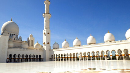 Fototapeta na wymiar Scheich-Zayid-Moschee in Abu Dhabi aus weißem Marmor, Kuppeln und Minarett unter blauem Himmel