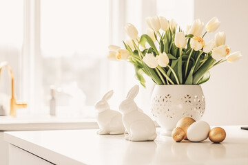 Easter table setting with tulips, Easter bunnies, and eggs with golden patterns in the white Scandinavian-style kitchen background. Beautiful minimalist design for greeting card