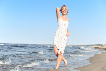 Fototapeta na wymiar Happy blonde beautiful woman having fun on ocean beach while dancing in waves