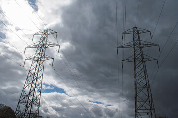 An pair of electricity pylons against a cloudy sky. Light catches the left pylon but leaves the right pylon in dark shadow. Strong contrast electricity grid picture of power distribution.