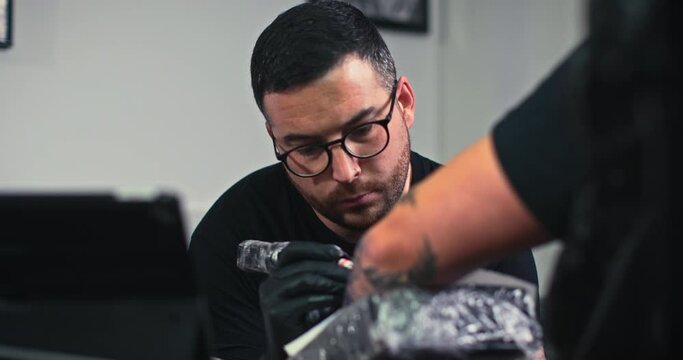 Close up tattoo artist shows the process of getting black tattoos with paint. The master works in black sterile gloves. Master tattoo artist in studio.