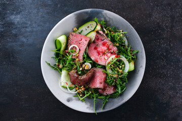 Traditioneller Commonwealth Sonntagsbraten als Aufschnitt Roastbeef mit Zucchini und Zwiebelringen in Rucola Salat serviert als Draufsicht in einer Design Schale 
