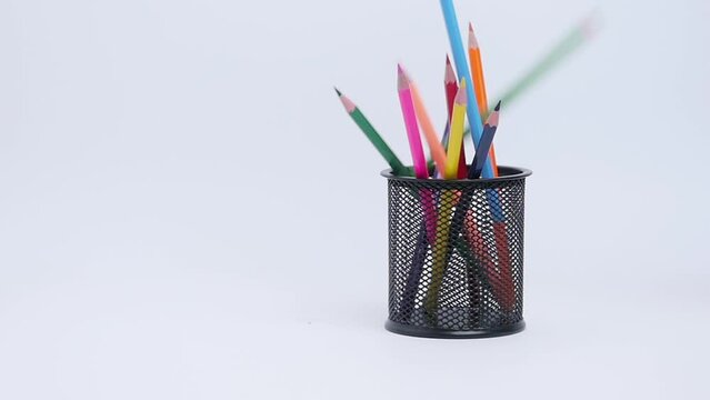 Multicoloure wooden pencils for drawing fall down in black metal pen holder, one falls on white surface, concept of missing target, school supplies, stationery. Close up, 4K Ultra HD.