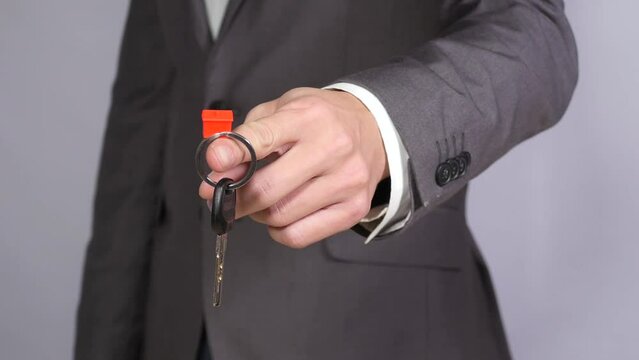 Man in grey suit holds key with little red figure of house, real estate, buying house, new accommodation, realtor. Close up, 4K Ultra HD.