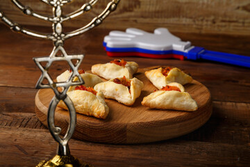 Fototapeta na wymiar gometashi triangles cookies with mishloach manot jam for Purim laid out on a wooden board next to the menorah rattles and whistle.