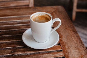 A large hot Americano in a white cup against the background of a wooden table. Strong coffee for breakfast