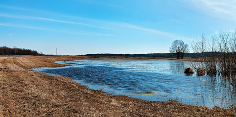 Early spring, river flood on agricultural meadows. Reflection in submerged fields covered by water. Seasonal overflow. Rural sunny Panorama.