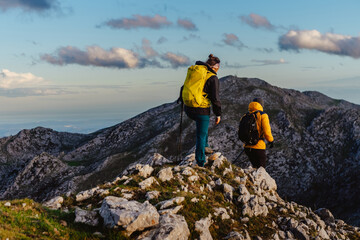 group of two mountaineers with backpack and trekking poles hiking up a mountain peak. sport, adventure and outdoor activity. weekend activities.