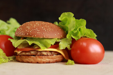 Cheeseburger with chicken cutlet close-up. Burger with cutlet, melted cheese, salad and vegetables. Fast food on a dark background