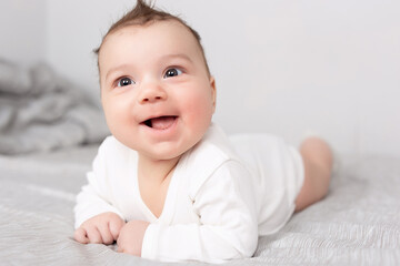The baby lies on his stomach on the bed. A beautiful baby smiles. Mockup for advertising, design, celebration, postcards.